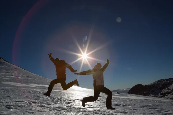 Silhouette couple jumping on snow against sun and blue sky — Stock Photo, Image