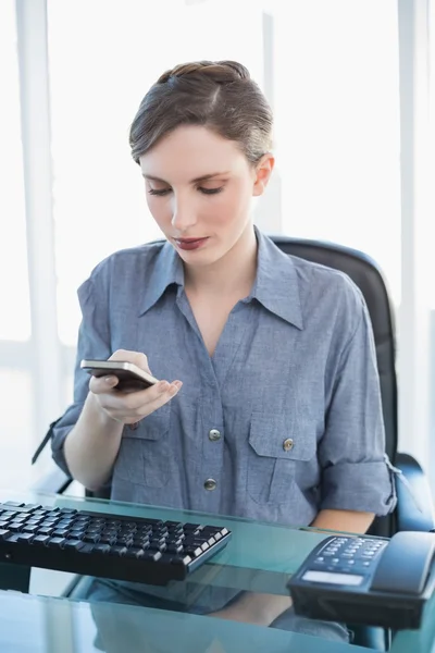 Ung affärskvinna med sin smartphone som sitter vid hennes skrivbord — Stockfoto