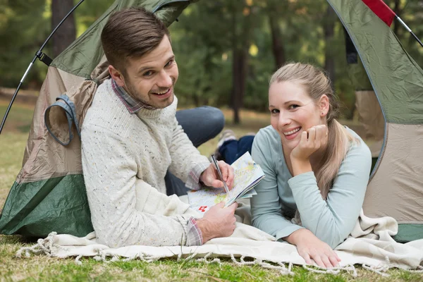 Smiling couple with a map lying in tent — Stock Photo, Image