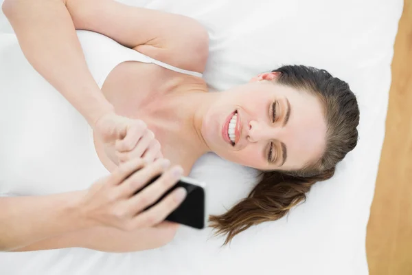 Mujer sonriente usando teléfono móvil en la cama — Foto de Stock
