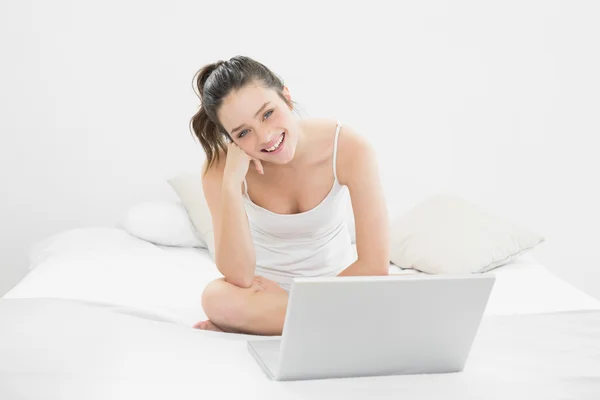 Sorridente donna casuale utilizzando il computer portatile a letto — Foto Stock