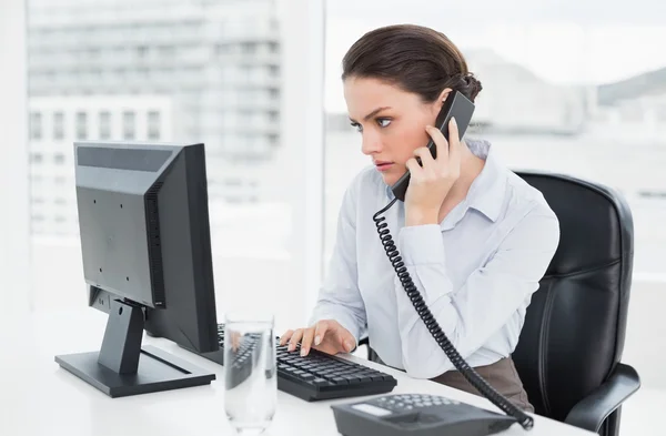 Elegante donna d'affari che utilizza telefono fisso e computer in ufficio — Foto Stock