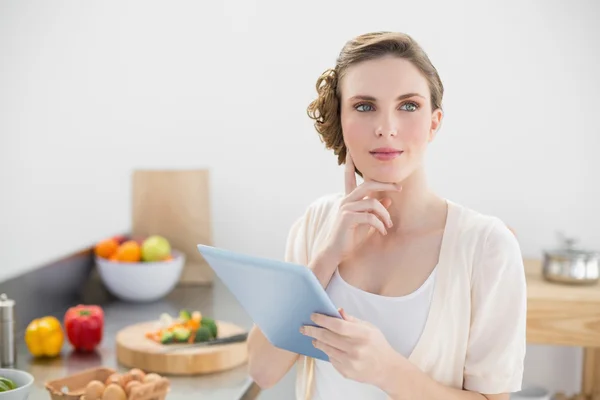 Junge nachdenkliche Frau steht in der Küche und hält ihr Tablet in der Hand — Stockfoto