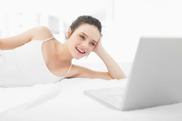 Smiling casual woman looking at laptop in bed — Stock Photo, Image