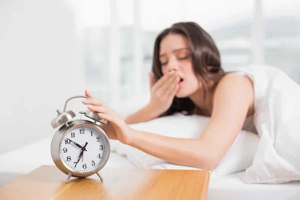 Mujer bostezando mientras extiende la mano al reloj despertador —  Fotos de Stock