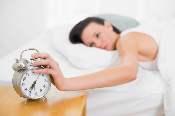 Женщина в постели протягивает руку к будильнику — стоковое фото