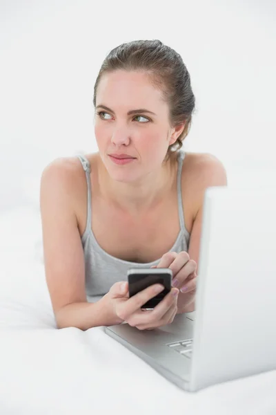 Mujer con teléfono celular y portátil tumbado en la cama — Foto de Stock