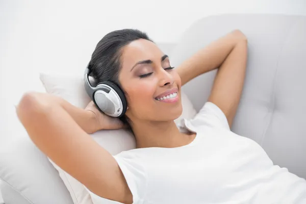 Niedlich lächelnde Frau auf dem Sofa liegend, während sie Musik hört — Stockfoto