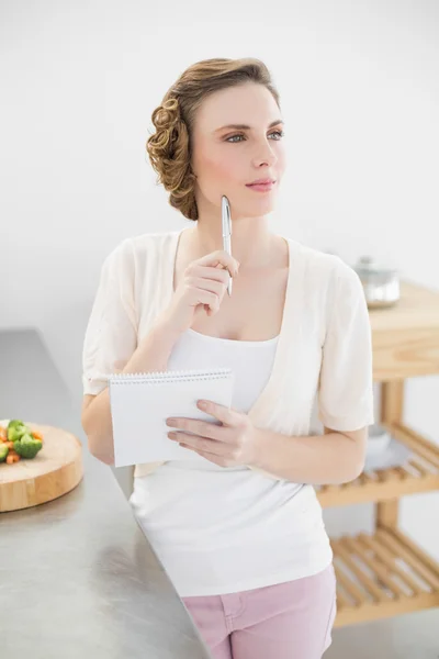 Thinking woman standing in kitchen writing a shopping list — Stock Photo, Image