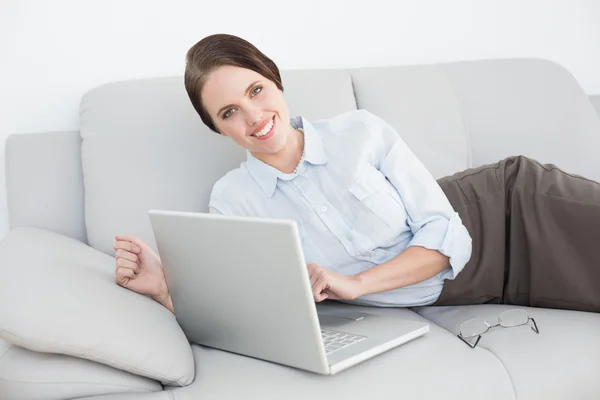 To se usmívám, dobře oblečená žena pomocí přenosného počítače na pohovce — Stock fotografie