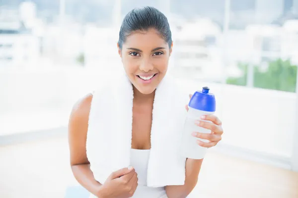 Sonriente morena tonificada con toalla sosteniendo botella deportiva —  Fotos de Stock