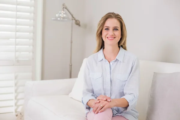 Casual happy blonde sitting on couch looking at camera — Stock Photo, Image