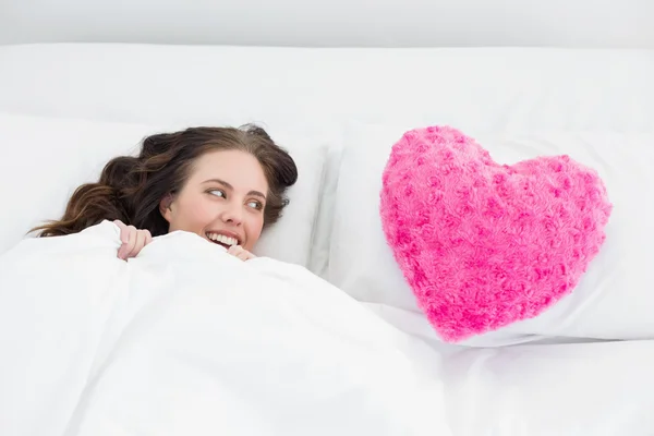 Woman lying in bed with heart shaped pillow cover — Stock Photo, Image