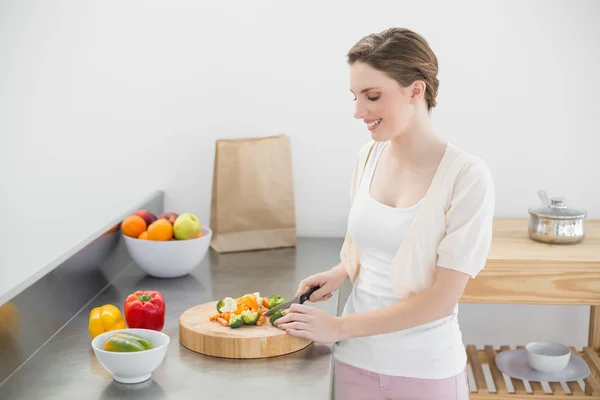 Fröhliche junge Frau schneidet Gemüse, während sie in ihrer Küche steht — Stockfoto