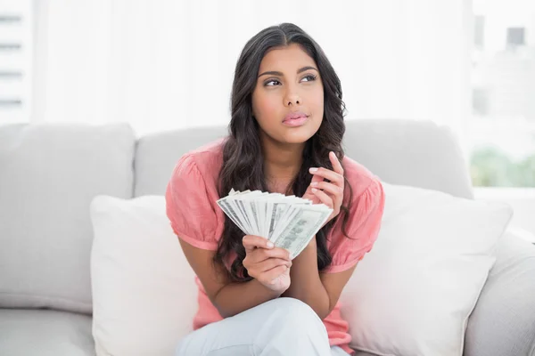 Promyšlené Roztomilá brunetka sedí na gauči, drží peníze — Stock fotografie