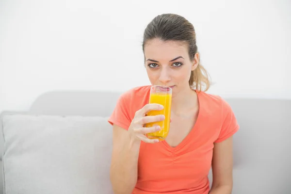 Prachtige rustige vrouw drinken van een glas sinaasappelsap camera kijken — Stockfoto