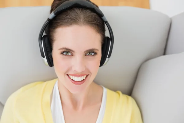 Smiling woman listening music through headphones on sofa — Stock Photo, Image