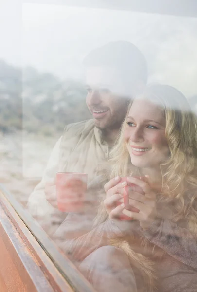 Thoughtful happy couple with coffee cups looking through window — Stock Photo, Image