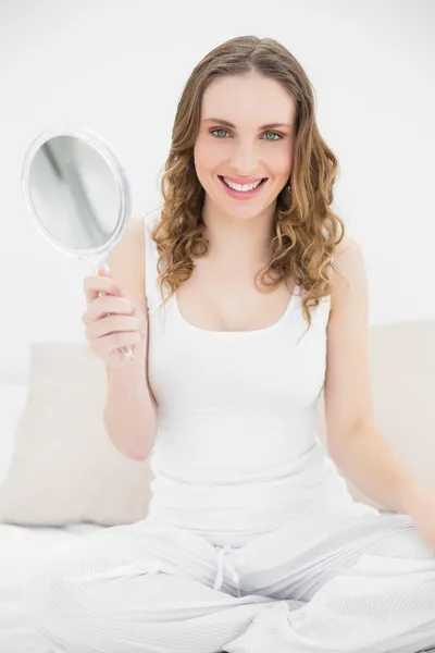 Young woman smiling into the camera and sitting on her bed — Stock Photo, Image