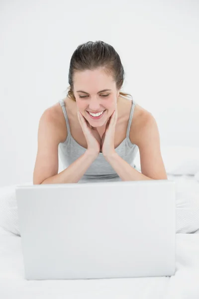 Smiling casual woman looking at laptop in bed — Stock Photo, Image