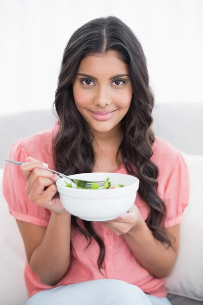 Verheugd schattige brunette zittend op bank holding slakom — Stockfoto