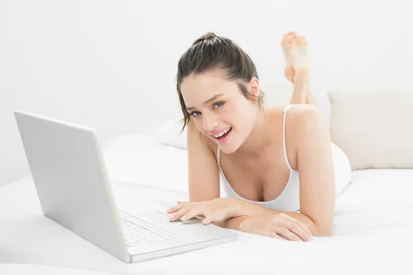 Sonriente mujer casual utilizando el ordenador portátil en la cama — Foto de Stock