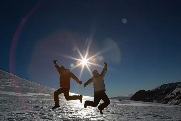 Silhouette couple jumping on snow against sun and blue sky — Stock Photo, Image