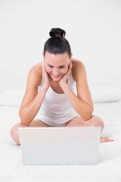 Lässig lächelnde Frau mit Blick auf Laptop im Bett — Stockfoto
