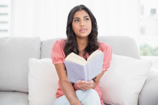 Thoughtful cute brunette sitting on couch reading a book — Stock Photo, Image