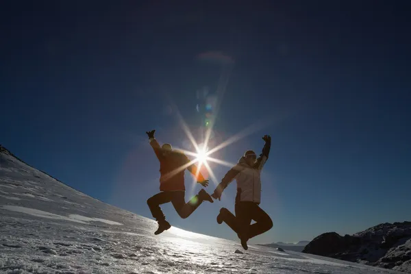 Silhouette couple jumping on snow against sun and blue sky — Stock Photo, Image