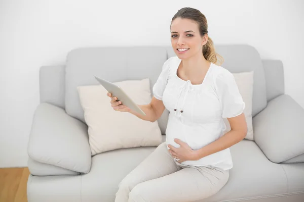 Mujer embarazada contenido sosteniendo su tableta sonriendo a la cámara — Foto de Stock