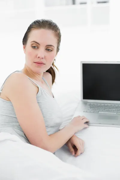Nachdenkliche, lässige Frau mit Laptop im Bett — Stockfoto