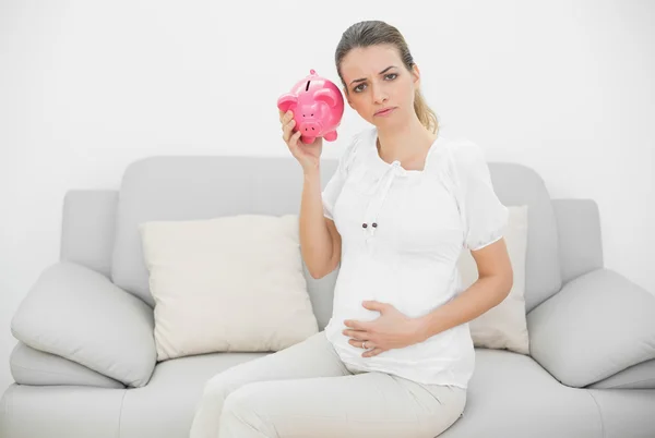 Deluso donna incinta scuotendo un salvadanaio rosa — Foto Stock