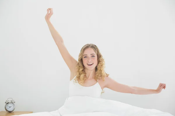 Bonita rubia sonriente sentada en la cama bostezando —  Fotos de Stock