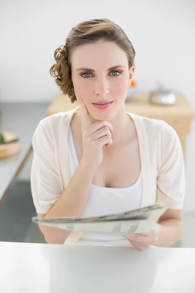 Mulher pensamento lindo sentado em sua cozinha segurando jornal — Fotografia de Stock