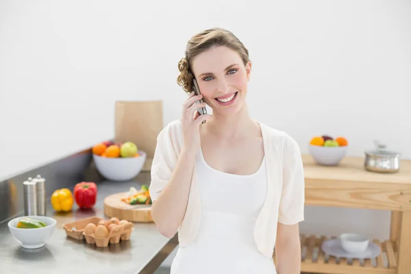 Joven alegre telefoneando con su teléfono inteligente de pie en la cocina —  Fotos de Stock