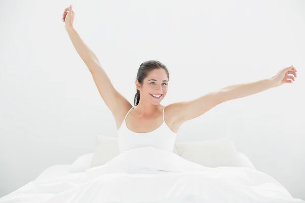 Mulher sorridente esticando os braços na cama — Fotografia de Stock