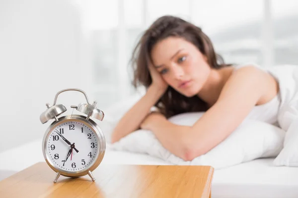 Sleepy woman looking at alarm clock on bedside table — Stock Photo, Image