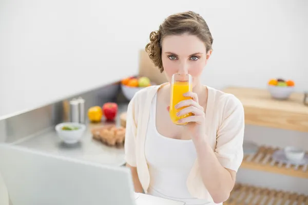 Mulher bonito beber um copo de suco de laranja sentado em sua cozinha — Fotografia de Stock