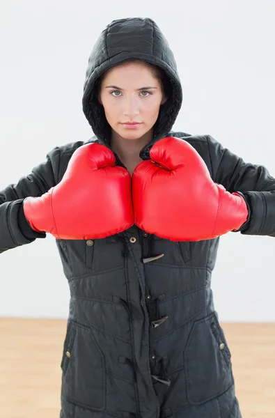 Serious woman in red boxing gloves and black hood at fitness stu — Stock Photo, Image