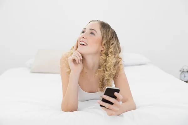 Vacker dag drömmer blond liggande på sängen med smartphone — Stockfoto