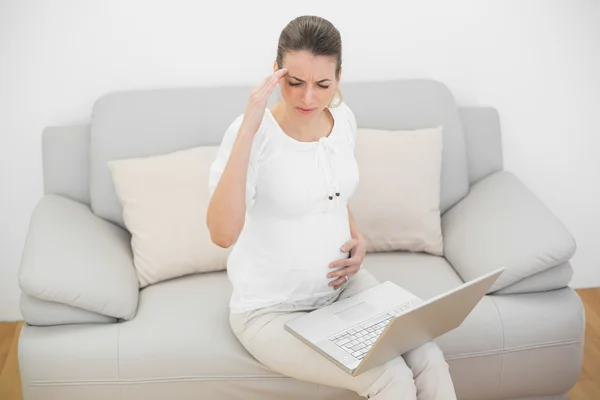 Mulher grávida com dor de cabeça tocando sua barriga sentada no sofá — Fotografia de Stock