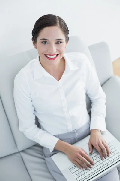 Sonriendo mujer joven bien vestida usando el ordenador portátil en el sofá — Foto de Stock