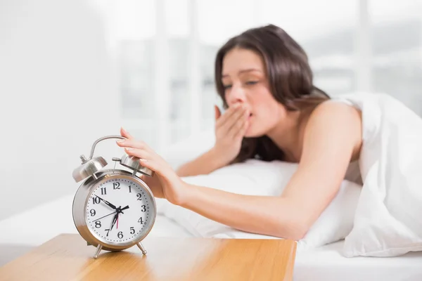 Frau gähnt, während sie Zeiger auf Wecker ausstreckt — Stockfoto