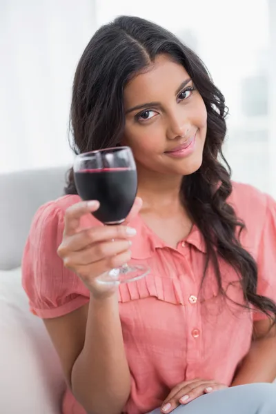 Улыбающаяся милая брюнетка сидит на диване, держа бокал вина — стоковое фото