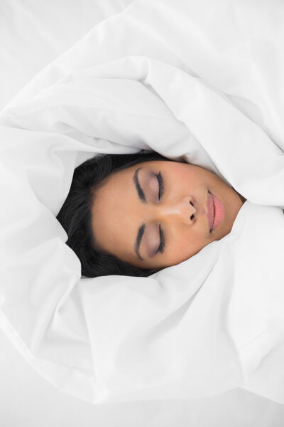 Красивая женщина спит под прикрытием на своей кровати
