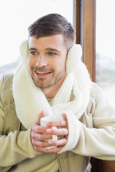 Man wearing earmuff with coffee cup against window — Stock Photo, Image