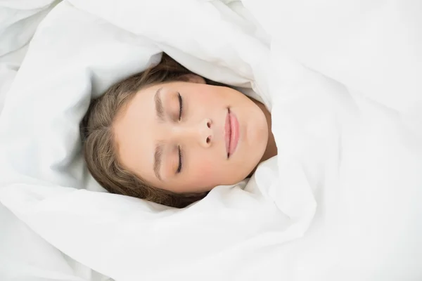 Bella donna sdraiata a dormire sotto la copertura sul suo letto — Foto Stock