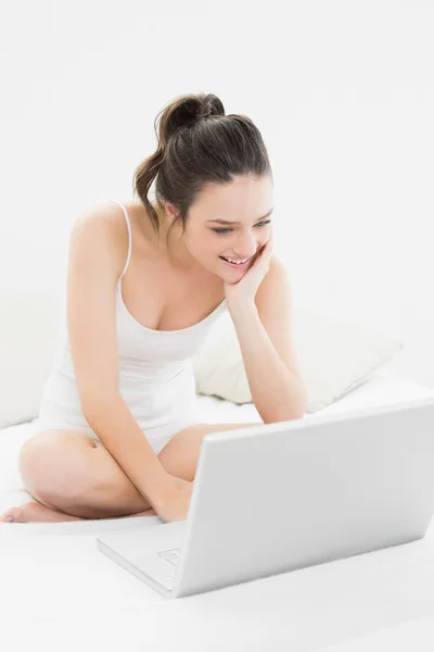 Sorridente donna casual con computer portatile sul letto — Foto Stock