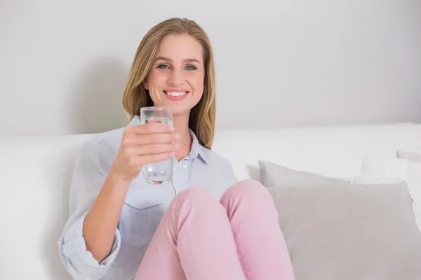 Smiling casual blonde sitting on couch holding glass of water — Stock Photo, Image